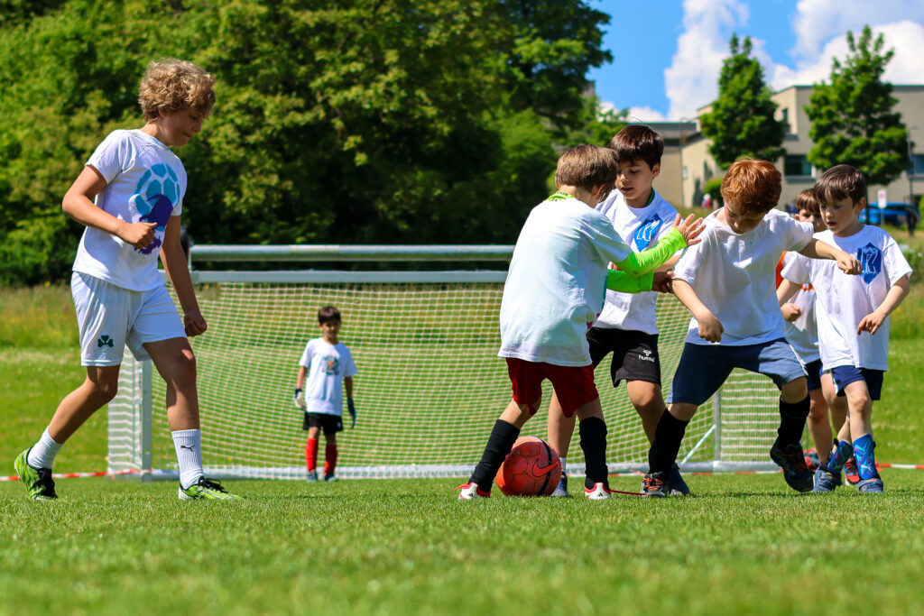 Kinder der Jungwacht beim Fussballspielen auf einer grünen Wiese.